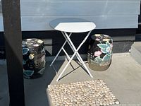 Overall view of folding table, two garden stools, pebble mat