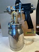 Left side view of Powermate spray gun showing handle branding, trigger, brass fittings and attached metal paint cup