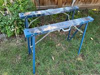 Two blue folding sawhorses set up on grass
