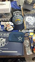 Overview of lot showing Rams banner and cap, Chargers cap and plush, Cowboys pouch and keychain, NFL binder, cheer sticks
