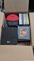 Open box showing CD wallets, stack of CD albums, cassette tapes and DVD sets