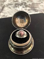 Ring displayed in small metal presentation box, top view showing stone and setting