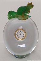 Front view of clear crystal clock with frog on top and visible quartz dial