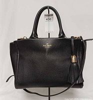 Front view of Kate Spade black pebbled leather satchel with tassel and logo