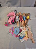 Barbie scooter, five dolls, clothing and accessories laid on surface