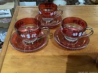 Set of three cranberry glass espresso cups with saucers shown together