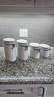 Front view of four white ribbed ceramic canisters with clamp lids