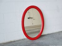Front view of red oval wall mirror leaning on wall