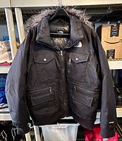 Front view of jacket on hanger showing pockets, faux-fur hood, rib hem