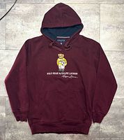 Front view of burgundy Polo Bear hoodie showing graphic, pocket, hood, cuffs, hem