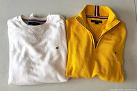 White and yellow Tommy Hilfiger pullovers folded on table