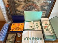 Assorted lot laid out: textiles, boxed tea set, lantern packaging, small framed embroidery, jade plant, cloisonné bird