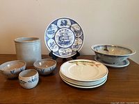 All items grouped on table: crock, Maine plate, berry bowl and plate, four dinner plates, two bowls, one cup