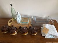 Full lot overview on table showing bakeware, cutting board, bottles, towels, soup bowls with lids