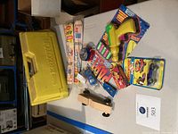 Tabletop view showing yellow Erector case, sealed glider kits, cap gun, cap rolls, confetti popper, loose and packaged cars