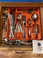 Drawer containing assorted cutlery pieces and orange plastic tray