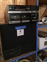 Stereo unit atop two black speakers with lot label visible