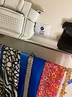 White perforated satchel bag, black evening bag, scarves and belts hanging on rack