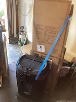 Boxed stainless steel step trash cans strapped together with blue straps, black shredder in foreground