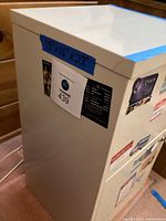 Side view of cream metal two-drawer filing cabinet showing dimension tape 15×16×28 and lot sticker