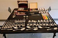 Overview of table with flatware rows, wood boxes of knives, packaged paring knives, server and forks