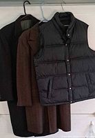 Two overcoats and quilted vest on hangers