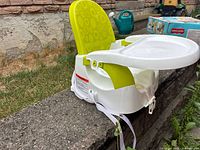 Side view of white booster seat with green backrest and tray showing straps