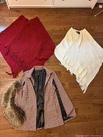 Overview of jacket, faux fur collar and two ponchos on floor
