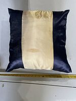 Front view of square navy blue and beige pillow with measuring tape showing width