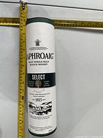 Full view of Laphroaig Select Scotch cylindrical box with tape measure showing height