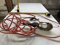 Full view of corded trouble light, protective cage with bulb, long orange cord, hook visible