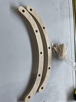 Two curved wooden arcs with drilled holes and a bag of dowels on tabletop, measuring tape visible for scale