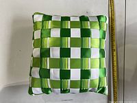 Front view of the green and white woven satin pillow beside measuring tape