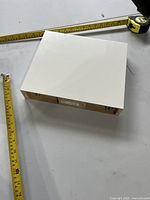 Top view of white Ikea floating shelf with tape measures showing dimensions and mounting hardware on back edge