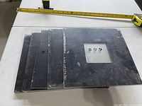 Stack of five black square mirrors with tape measure showing approx 10" width, protective film on some pieces