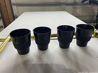 Four black Nespresso espresso cups aligned in a row with tape measure for scale