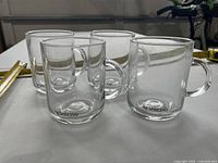Four clear Nespresso-branded glass mugs on table with measuring tape for scale