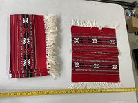 Stack of folded red woven placemats and one opened to show pattern and fringe with measuring tape for scale