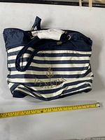 Front view of navy and white striped shoulder bag with measuring tape showing width