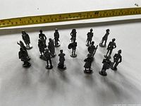 Seventeen small metal figurines with tape measure indicating height around 1.5-2 in.