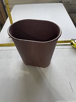 Brown oval plastic waste bin with tape measure showing dimensions