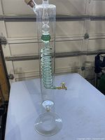 Full view of glass dispenser showing spiral coil, brass spigot, corked top, pedestal base