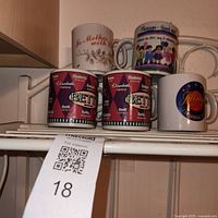 Shelf with five coffee mugs showing designs and lot tag