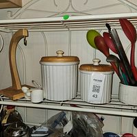 Shelf view showing wooden banana stand, two ceramic canisters, utensil crock with utensils