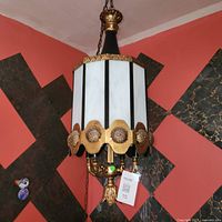 Full view of pendant chandelier hanging, showing shape, glass panels, filigree band, chain and ceiling canopy