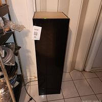 Full view of glossy black pedestal showing power cord and overall form