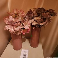 Two mauve plastic vases with faux flowers