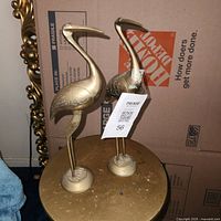 Front view of both brass flamingo statues on table