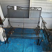 Front view of wrought iron two-seater glider bench showing mesh panels and scrollwork
