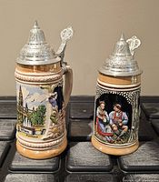 Front view showing both steins, relief artwork, and pewter lids